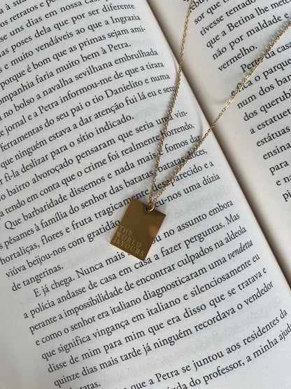 Colar dourado, com pendente retangular, com a frase "The World is Yours".